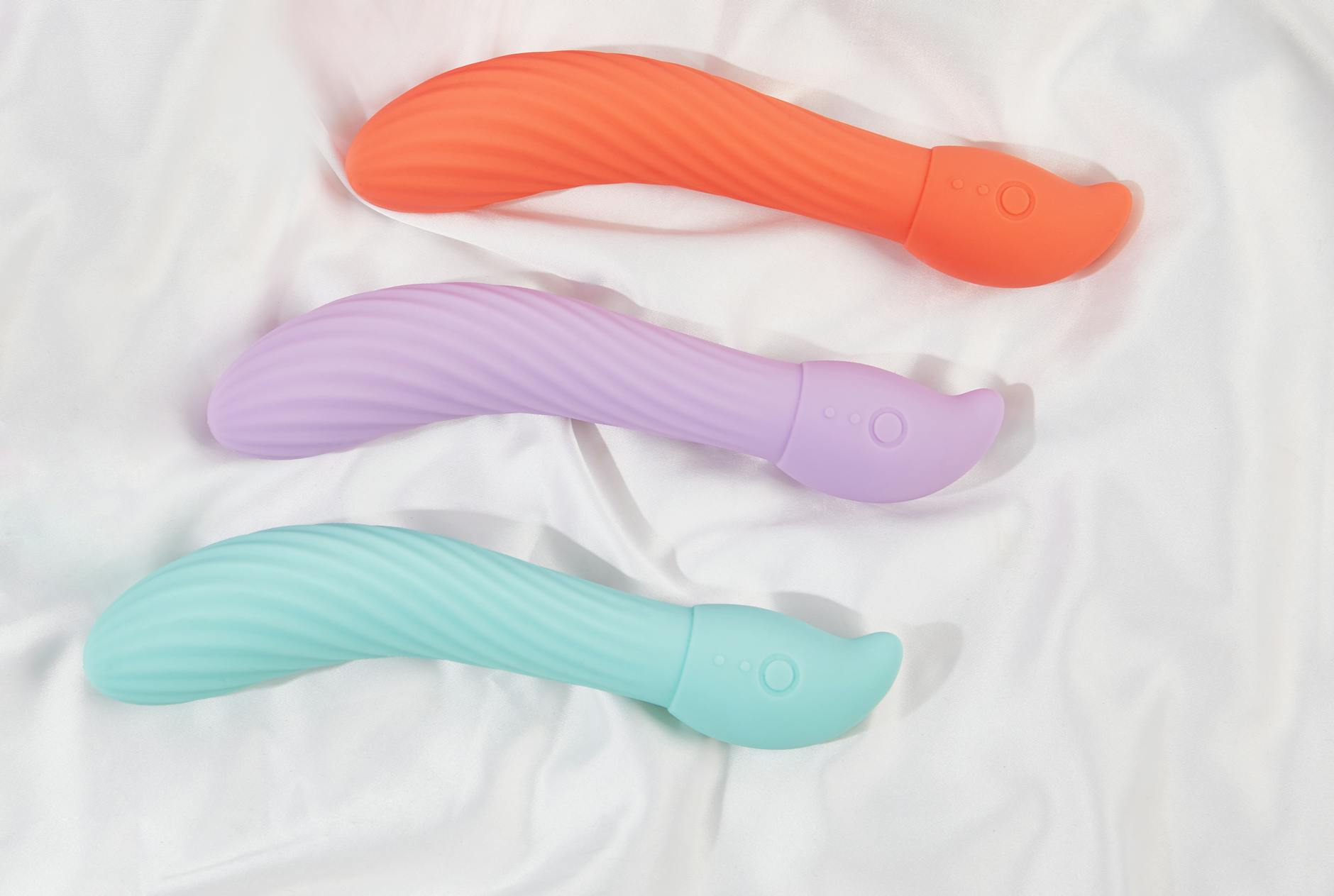 Three colorful clitoral vibrators arranged on white fabric