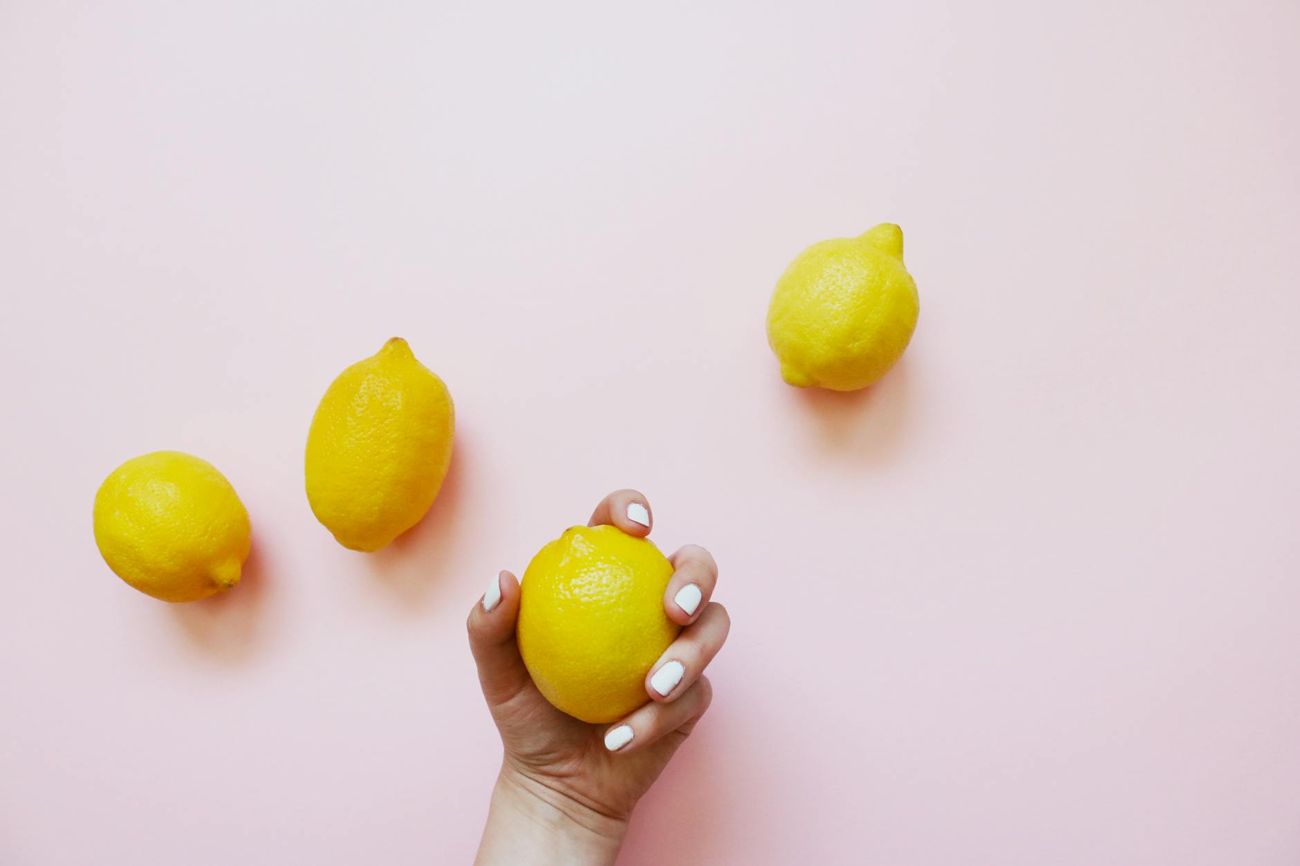 A hand holding a fresh lemon on a soft pink background, representing pleasure reclamation and self-care