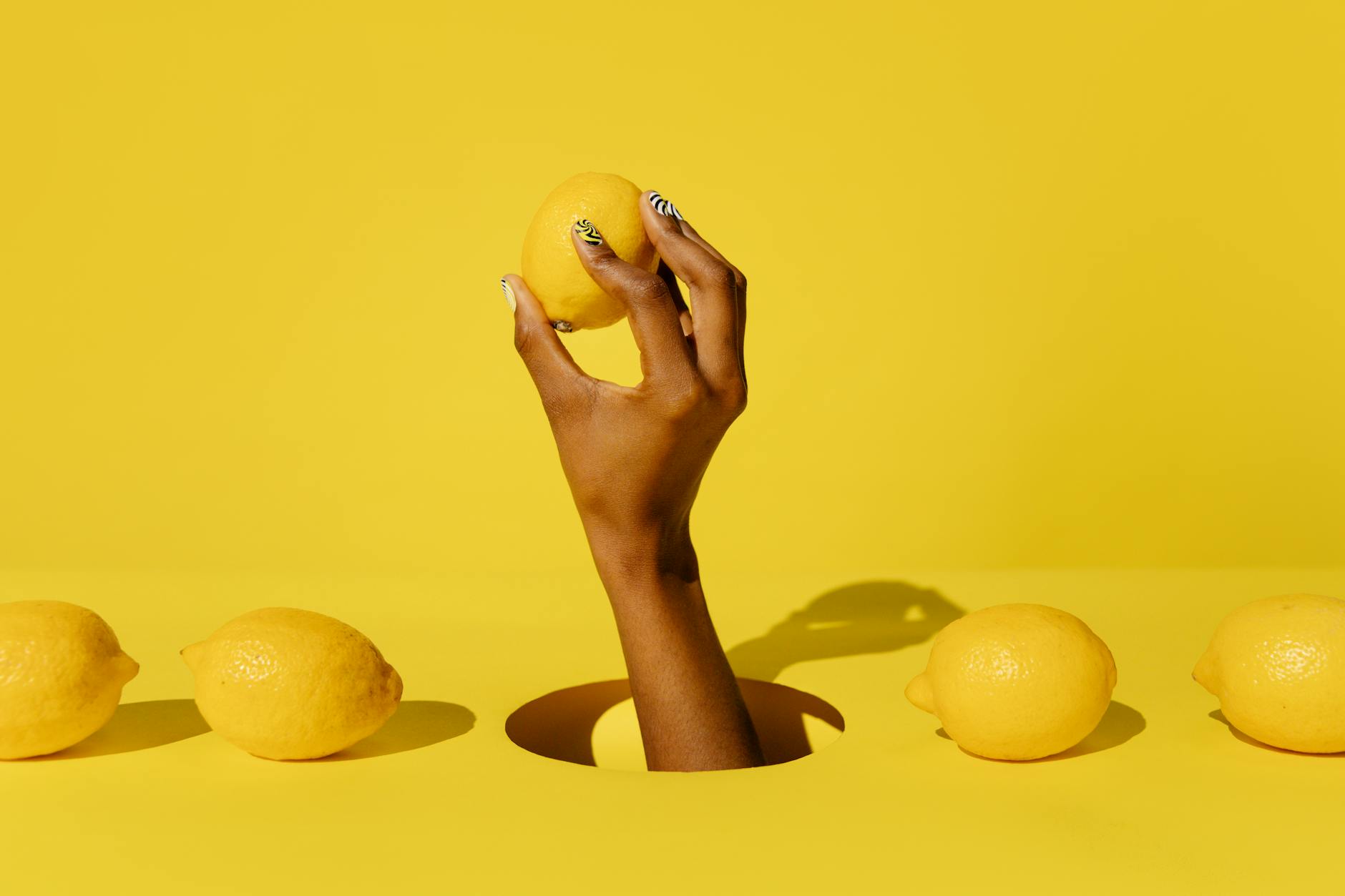 A hand holding a fresh yellow lemon against a vibrant yellow background, symbolizing natural pleasure and citrus freshness