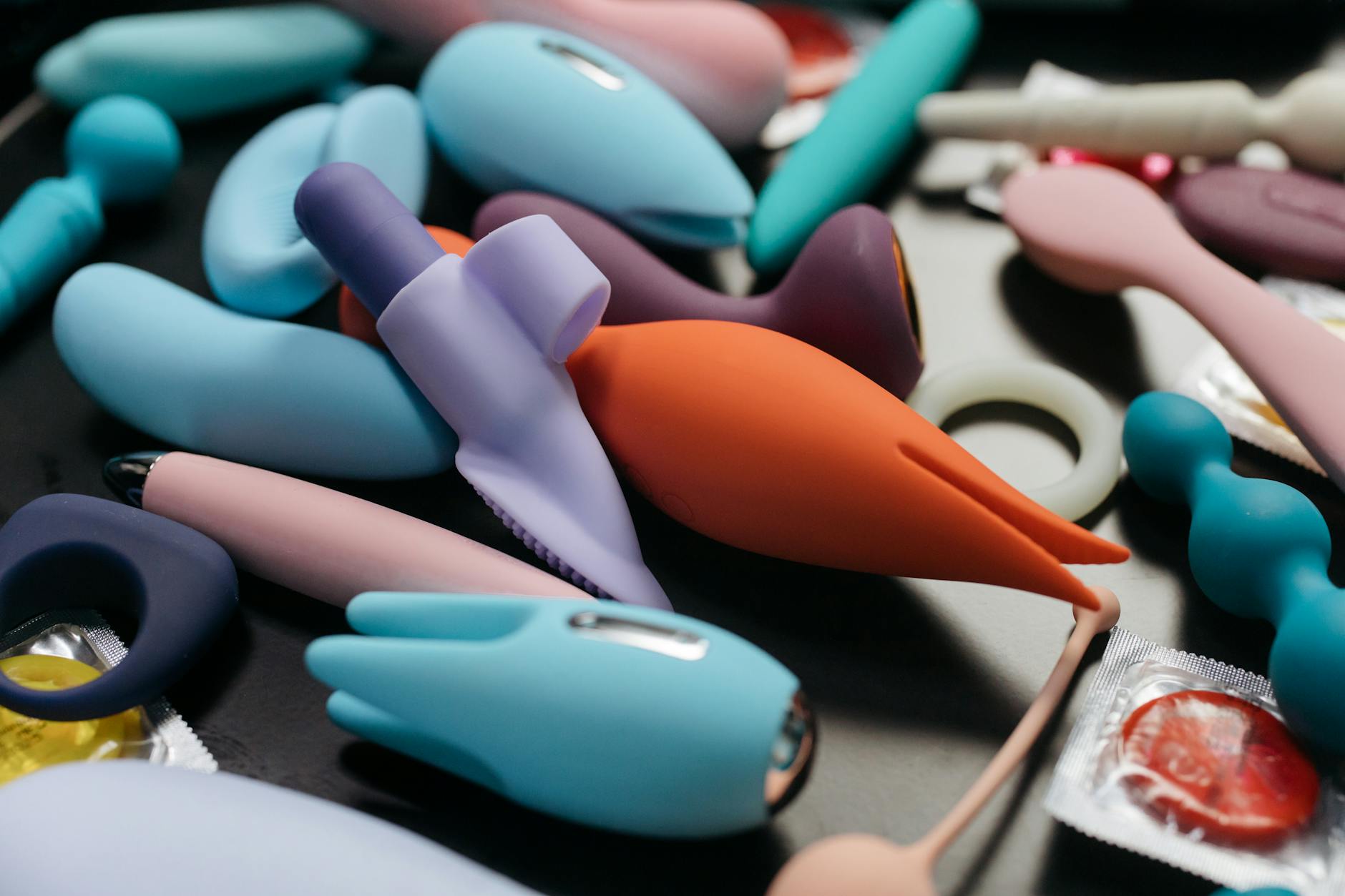 Two hands holding pink and blue silicone vibrators against a pastel background