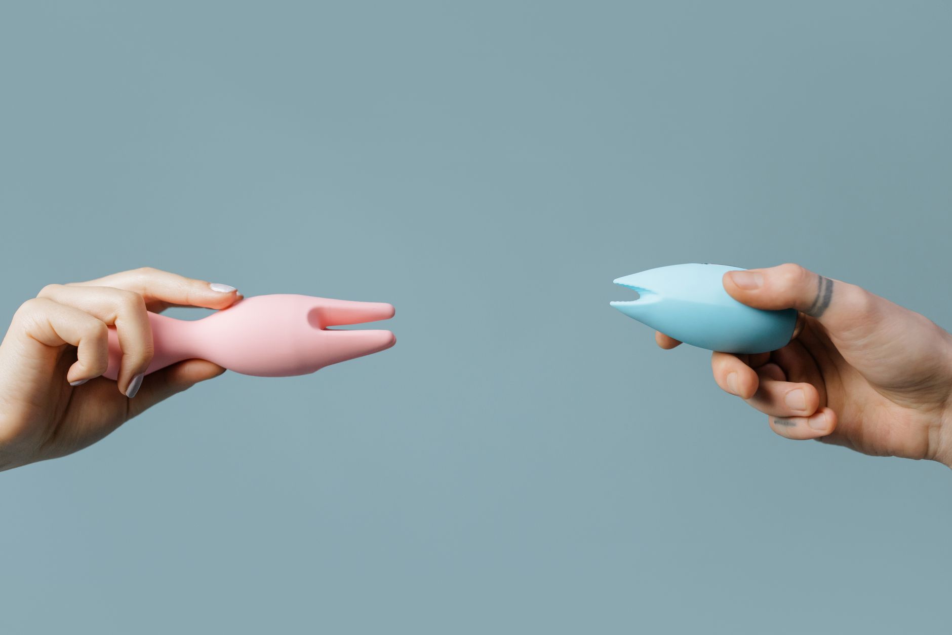 Two hands holding pastel-colored silicone vibrators together in collaborative intimacy