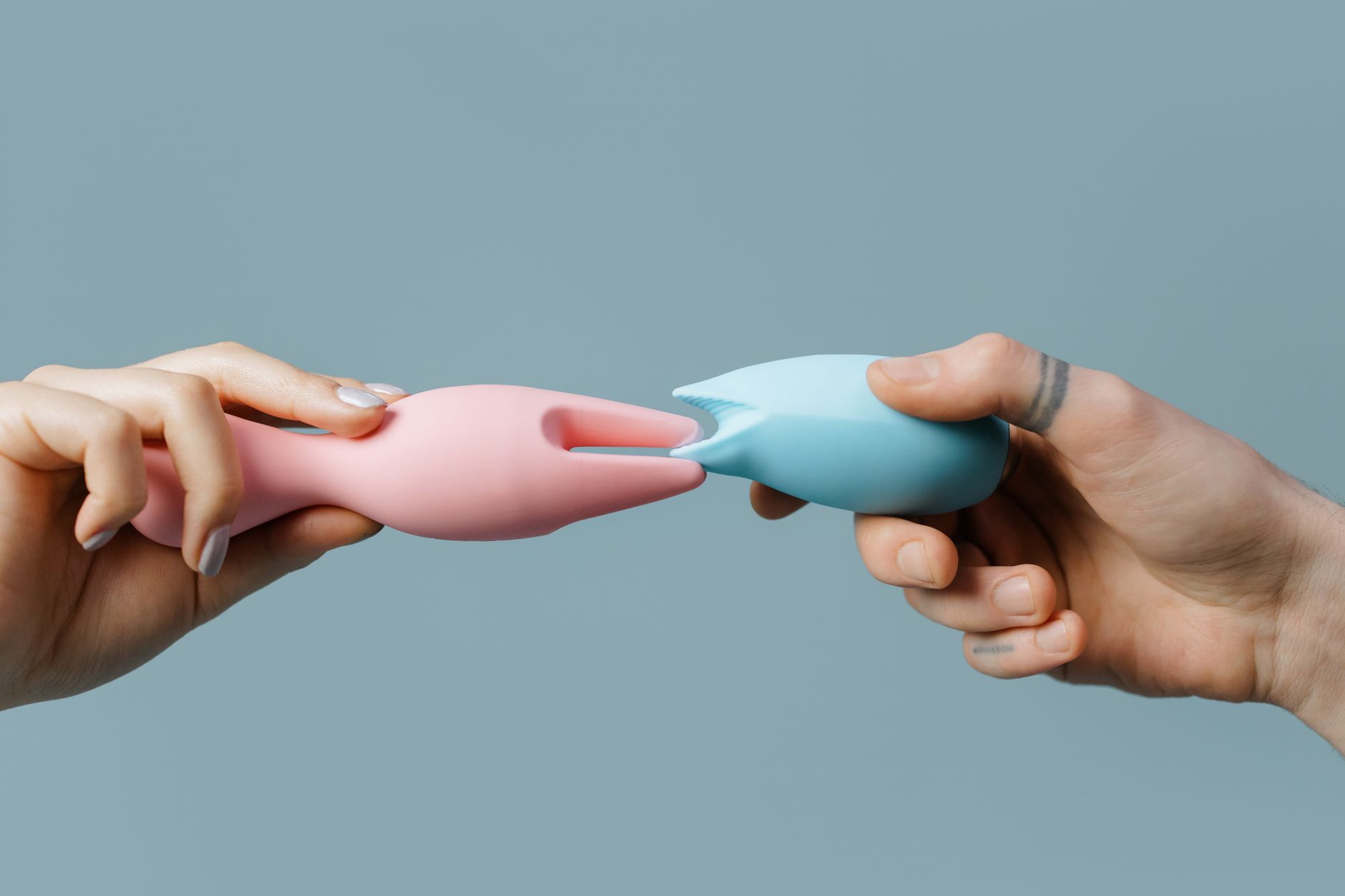Hands holding a collection of colorful silicone vibrators and adult toys