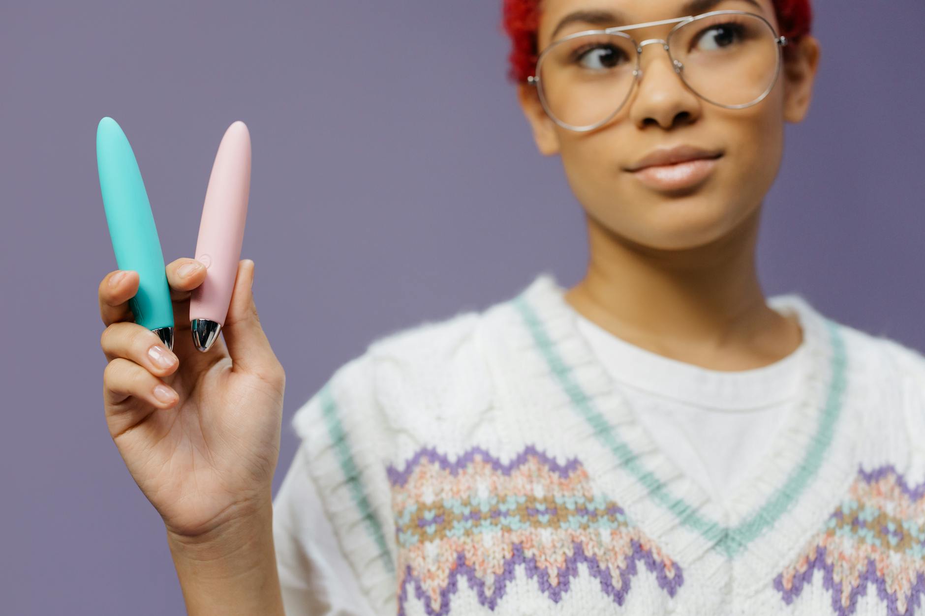 Woman holding blue and pink silicone clitoral vibrators in a thoughtful pose